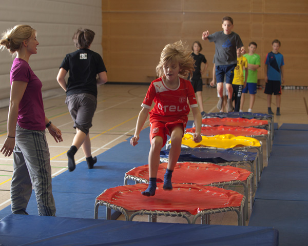 Kinder springen im Sportunterricht auf Minitrampolinen.