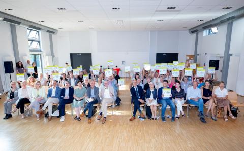 Gruppenbild, Schulleitungen sitzen in der Gemeinschaftsgrundschule Lustheider Straße Köln die Startchancen-Plaketten in die Höhe.