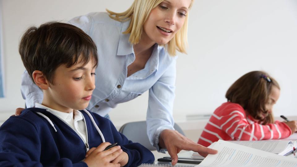 Lehrerin erklärt einem Schüler Unterrichtsstoff mithilfe eines Buches Lehrerin erklärt einem Schüler Unterrichtsstoff mithilfe eines Buches