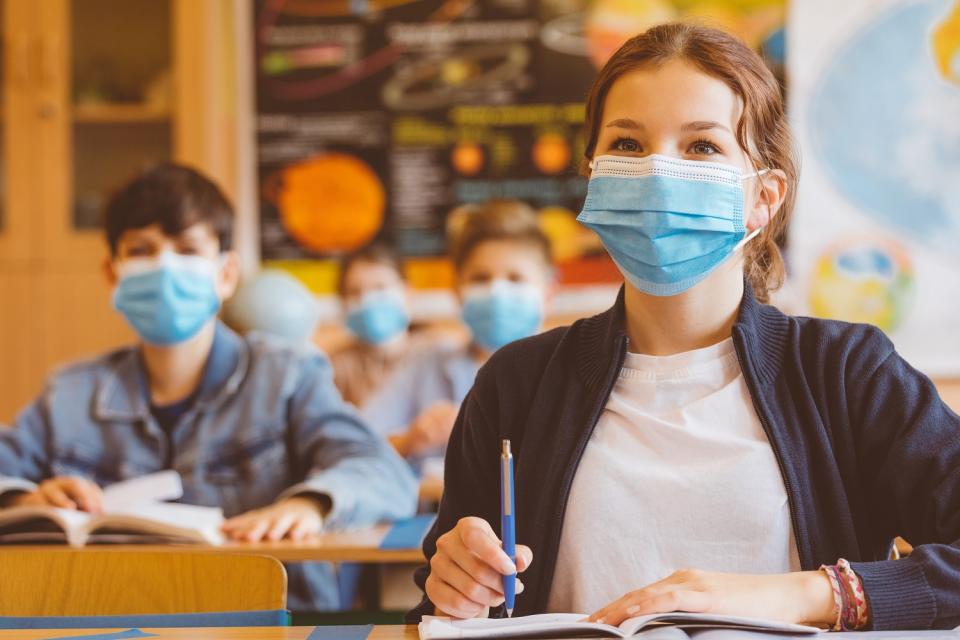 Schülerin sitzend mit Heft und Stift mit Maske im Klassenverband Schülerin sitzend mit Heft und Stift mit Maske im Klassenverband