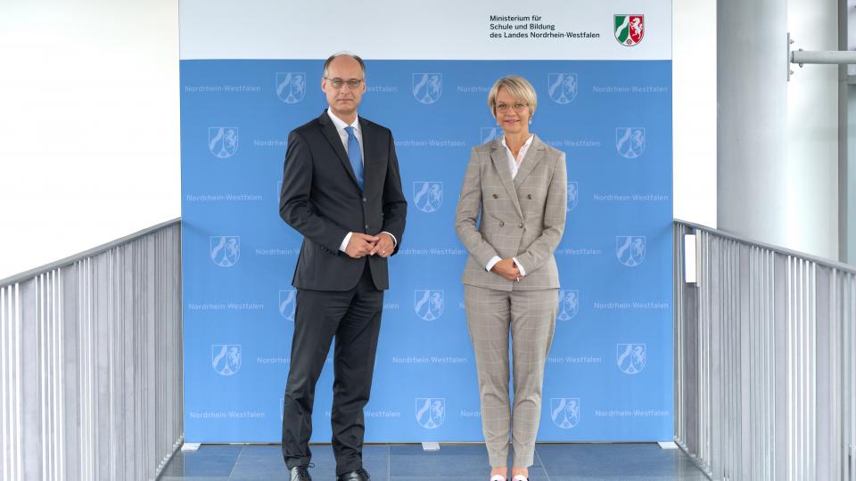 Ministerin Feller und Staatssekretär Mauer stehen nebeninander vor einer Stellwand des MSB
