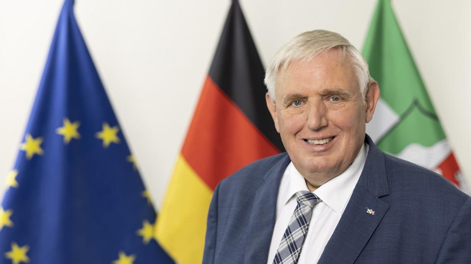 Minister Karl Josef-Laumann steht vor den Flaggen von Europa, Deutschland und NRW.