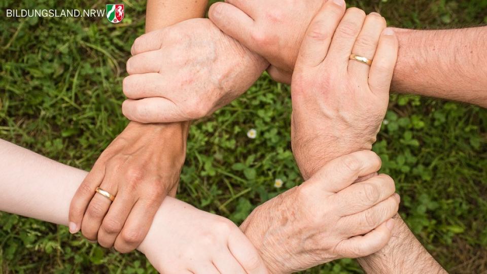 Hände verschiedener Generationen sind über einer Rasenfläche zu einem Geflecht verschränkt