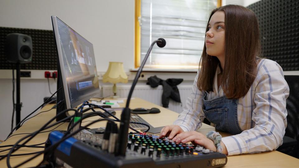 Ein Mädchen sitzt in einem Tonstudio vor einem Bildschirm.