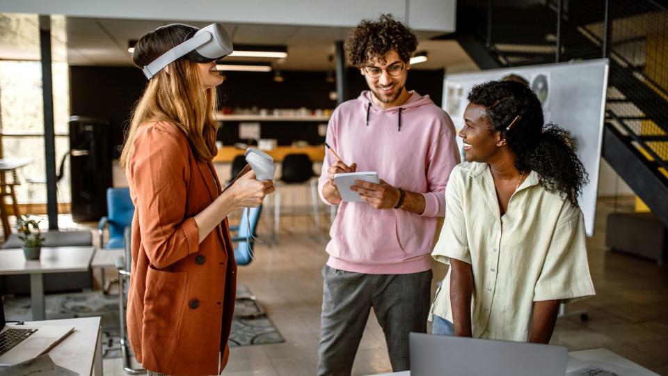 Drei junge Menschen arbeiten mit verschiedenen Medien, unter anderem mit einer VR-Brille.