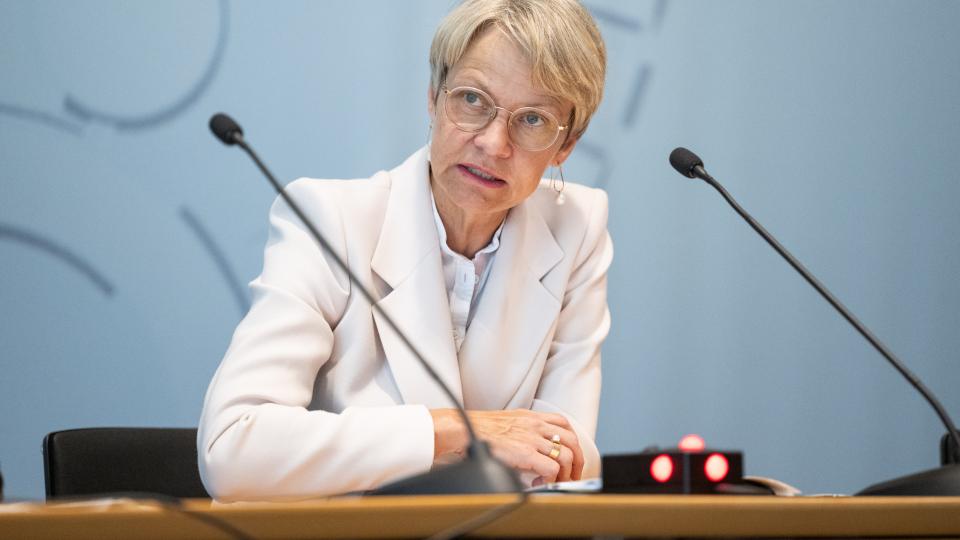 Ministerin Dorothee Feller sitzt an einem Tisch hinter zwei Mikrofonen und spricht.