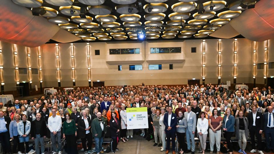 Gruppenbild von 400 Schulleiterinnen und Schulleitern der Startchancen-Schulen. In der Mitte wird ein Schild hochgehalten, auf dem steht: "Wir sind eine Startchancen-Schule!" (24. Juni 2024)