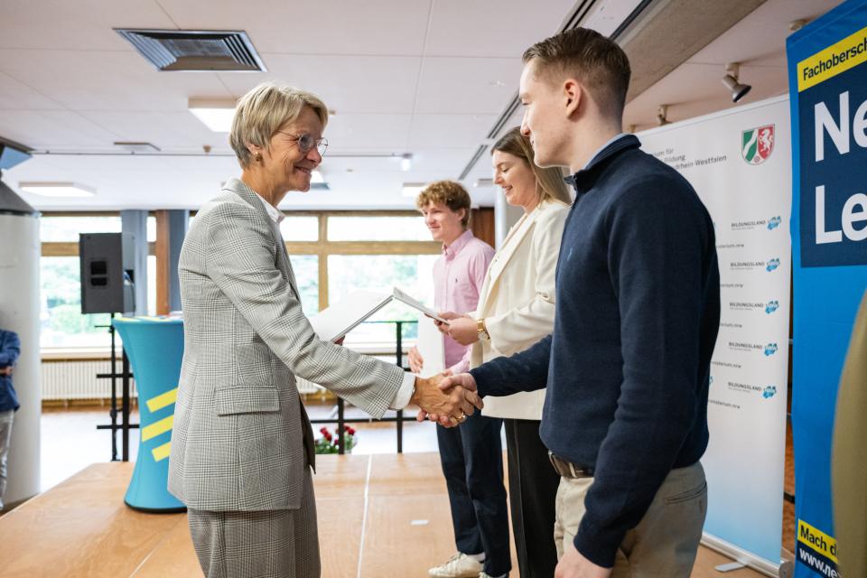 Ministerin Dorothee Feller im Gespräch mit einer Absolventin der FOS-Polizei, die ihr Abschlusszeugnis in der Hand hält.