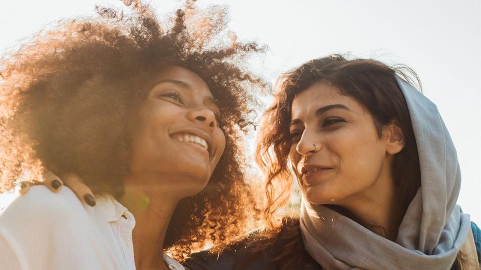 Zwei Frauen mit Migrationshintergrund stehen eng beisammen, eine der beiden trägt ein lockeres Kopftuch.