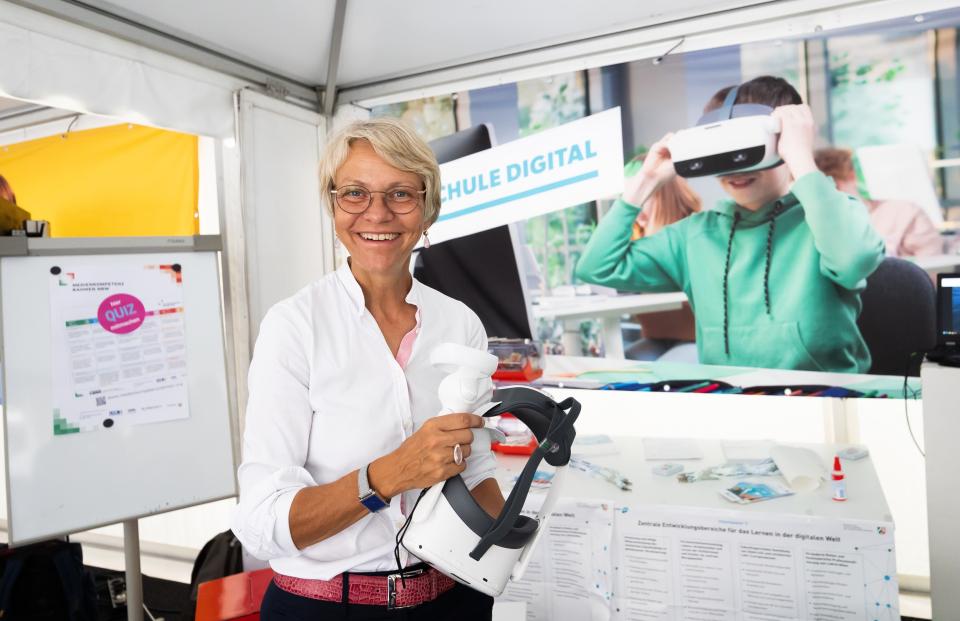 Ministerin Feller hat eine VR-Brille in der Hand.