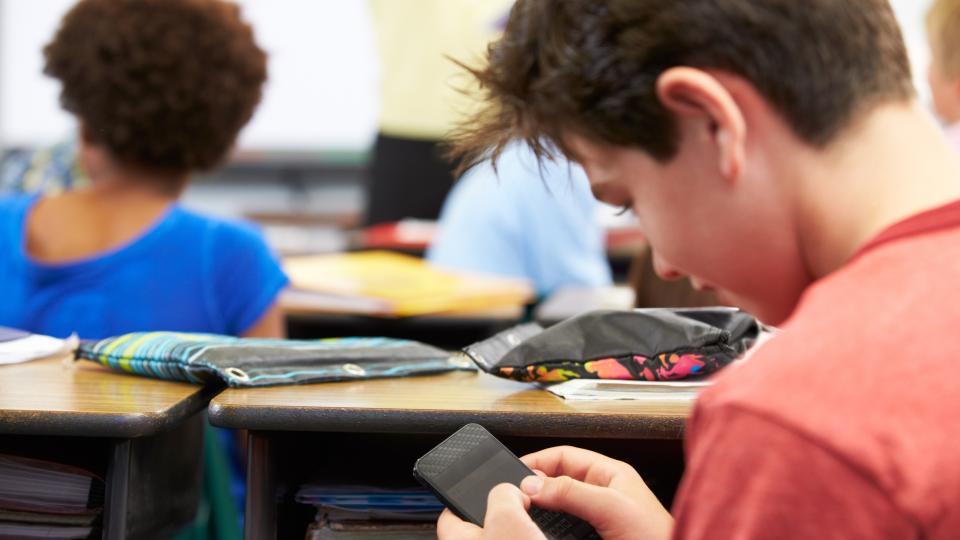 Ein Schüler sitzt im Unterricht und blickt auf das Handy in seiner Hand.