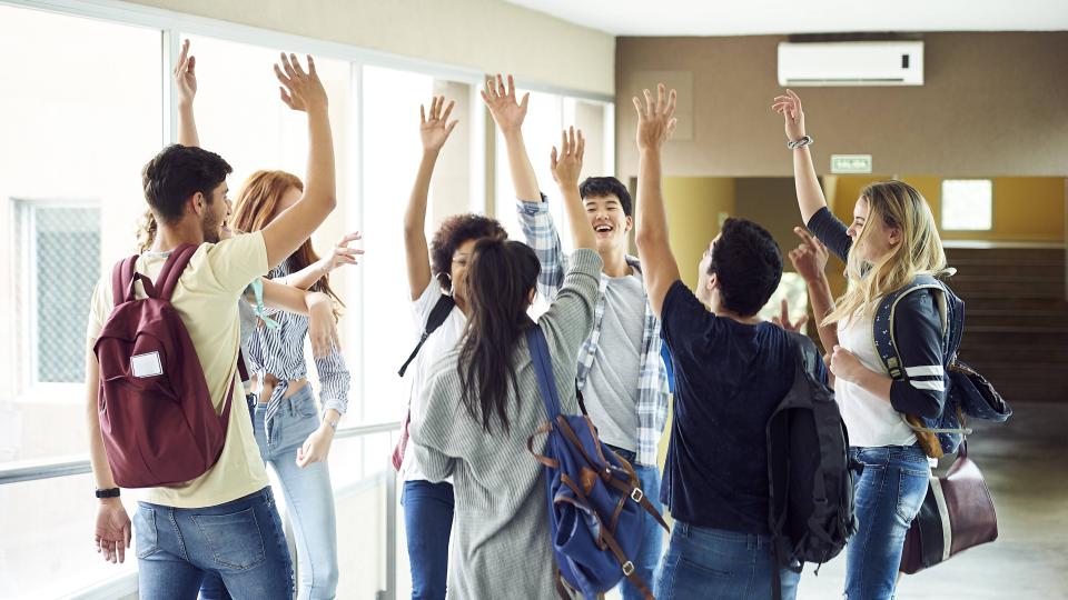 Eine Gruppe Schüler steht in einem Schulflur und hat die Hände zum "High Five" erhoben.