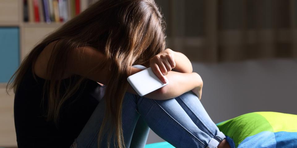 Mädchen hockt auf einem Bett, den Kopf auf die Knie gestützt, in der Hand ein Smartphone. Mädchen hockt auf einem Bett, den Kopf auf die Knie gestützt, in der Hand ein Smartphone.