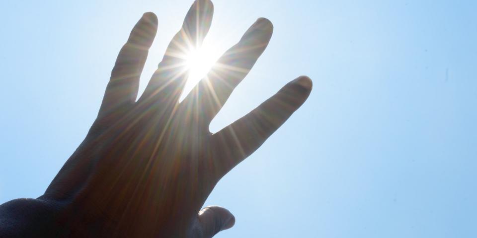 Eine linke Hand vor blauem Himmel, durch die Finger blinzelt die Sonne hindurch. Eine linke Hand vor blauem Himmel, durch die Finger blinzelt die Sonne hindurch.
