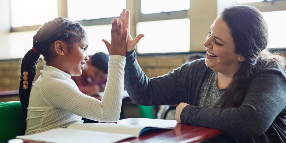 Schülerin und Lehrerin berühren ihre Hände in einer "High Five"-Geste. Beide lächeln dabei. Schülerin und Lehrerin berühren ihre Hände in einer "High Five"-Geste. Beide lächeln dabei.