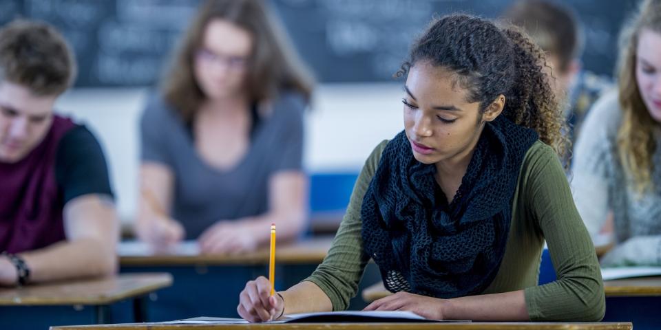 Jugendliche sitzen in einem Klassenraum an Tischen und schreiben. Jugendliche sitzen in einem Klassenraum an Tischen und schreiben.