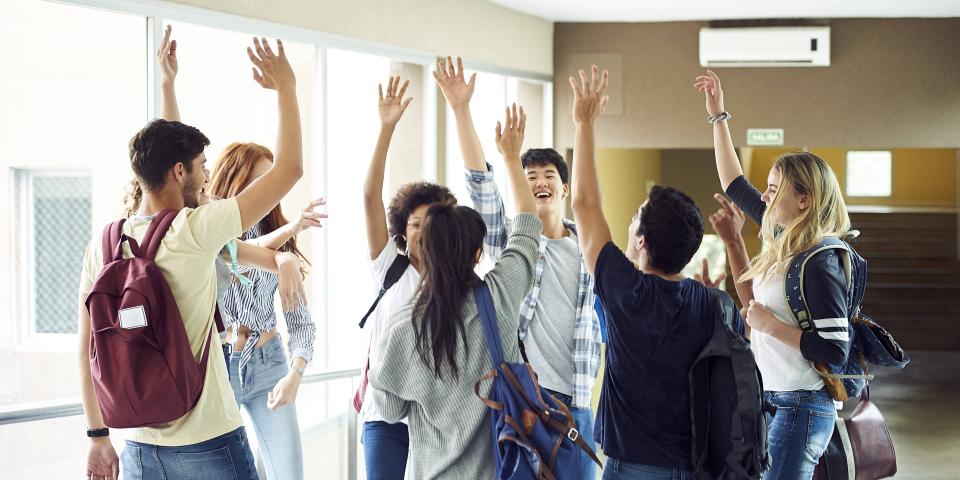 Eine Gruppe Schüler steht in einem Schulflur und hat die Hände zum "High Five" erhoben. Eine Gruppe Schüler steht in einem Schulflur und hat die Hände zum "High Five" erhoben.