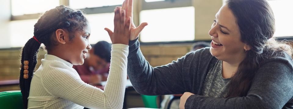 Schülerin und Lehrerin berühren ihre Hände in einer "High Five"-Geste. Beide lächeln dabei. Schülerin und Lehrerin berühren ihre Hände in einer "High Five"-Geste. Beide lächeln dabei.