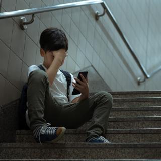 Junge sitzt mit seinem Smartphone in der Hand auf einer Treppe