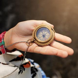 Ein Kompass wird in der geöffneten Hand eines jungen Menschen gehalten.