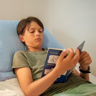 Ein Junge liegt in einem Krankenbett und liest in einem Buch