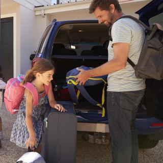 Eine Familie packt Koffer und Taschen in den Kofferraum eines Autos.