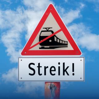 Straßenschild vor blauem Himmel mit der grafischen Darstellung eines durchgestrichenen Zuges. Darunter steht auf einem Schild "Streik!".