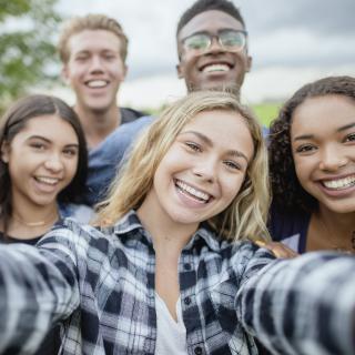 Selfie-Perspektive auf mehrere junge Menschen, die sich lächelnd zum Foto gruppiert hat.