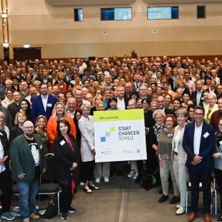 Gruppenbild von 400 Schulleiterinnen und Schulleitern der Startchancen-Schulen. In der Mitte wird ein Schild hochgehalten, auf dem steht: "Wir sind eine Startchancen-Schule!" (24. Juni 2024)