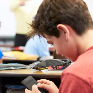 Ein Schüler sitzt im Unterricht und blickt auf das Handy in seiner Hand.