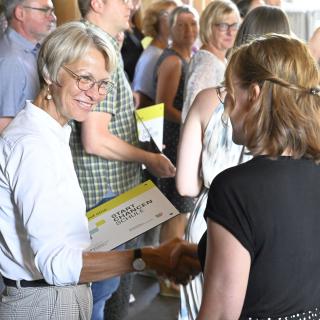 Ministerin Dorothee Feller überreicht einer Schulleiterin eine Startchancen-Plakette.