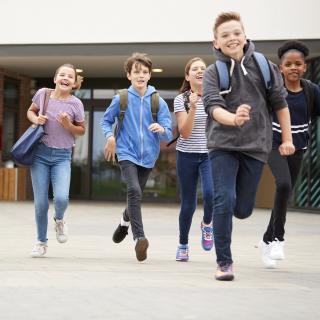 Gruppe von Schülerinnen und Schülern verlässt fröhlich rennend ein Schulgebäude.
